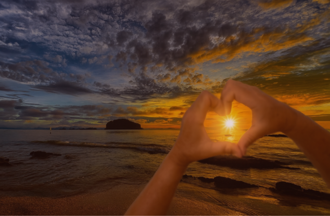 a beach sunrise with two hands making the heart symbol
